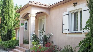 Una casa con facciata intonacata, persiane bianche e un portico coperto con gradini che conducono all'ingresso.