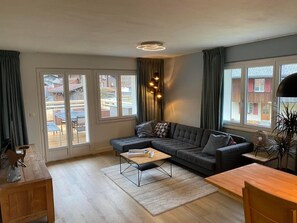A modern living room with a sectional sofa, a wooden coffee table, and a large window with curtains.