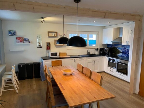 A modern kitchen with white cabinets, a wooden dining table, and black pendant lights.