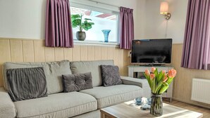 Ein Wohnzimmer mit einer Couch, einem Fernseher, einem Holztisch und einer Vase mit Blumen.