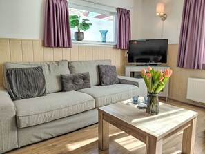 A living room with a sofa, a TV, a wooden coffee table, and a vase with flowers. - Sommerhaus in ruhiger Lage mit privatem Garten und Terrasse by Interhome (Egmond aan Zee)