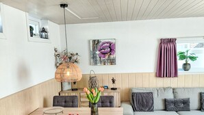 Ein modernes Wohnzimmer mit Essbereich, einer Couch, einem Tisch mit Stühlen, einer Hängelampe und einem Fenster mit Vorhängen.