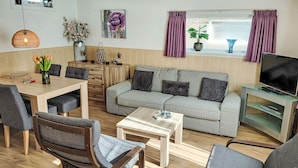 Ein Wohnzimmer mit Sofa, Sesseln, Couchtisch, TV-Möbel und einem Essbereich mit Tisch und Stühlen.