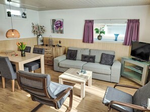 A living room with a sofa, chairs, a coffee table, a TV stand, and a dining area with a table and chairs. - Sommerhaus in ruhiger Lage mit privatem Garten und Terrasse by Interhome (Egmond aan Zee)