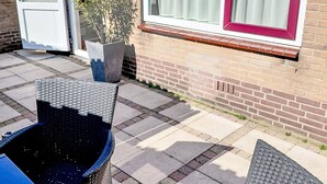 Eine Terrasse mit Gartenmöbeln, einem Topfpflanzen und einem Fenster mit Vorhängen.