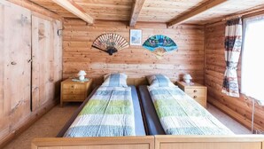 A wooden cabin room with two beds, wooden walls, a ceiling fan, and a window with curtains.