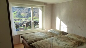 Ein Schlafzimmer mit zwei Betten, einem großen Fenster mit Blick auf ein Dorf und hellen Holzwänden.