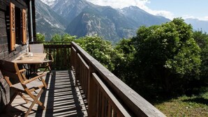 Terraza de madera con una mesa y sillas, con vistas a un paisaje montañoso.
