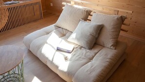 Una habitación acogedora con suelo de madera, un sofá con cojines, una mesita y una ventana con persianas.