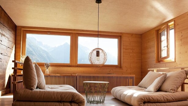 Una habitación acogedora con dos zonas de estar con cojines, una mesita y un ventanal con vistas a la montaña.
