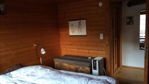 A wooden room with a bed, a radiator, and a door leading to another room.