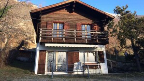 A wooden cabin with a balcony, large windows, and a front porch.