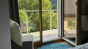 A bedroom with a large window offering a mountain view, a bed, a blue rug, and a chair with a pillow. - Chasa Stefania by Interhome (Scuol)