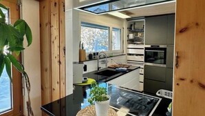 A modern kitchen with wooden paneling, a black countertop, white cabinets, and a view of the outdoors. - Chasa Stefania by Interhome (Scuol)