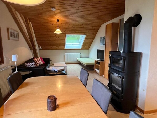 A cozy room with a wooden ceiling, a dining table, a sofa, a TV, and a wood stove. - Schafmatthof Dachwohnung by Interhome (Gänsbrunnen)