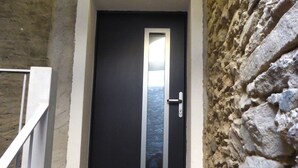 Eine schwarze Tür mit vertikalem Metallstreifen und Griff, in eine Steinmauer eingelassen.