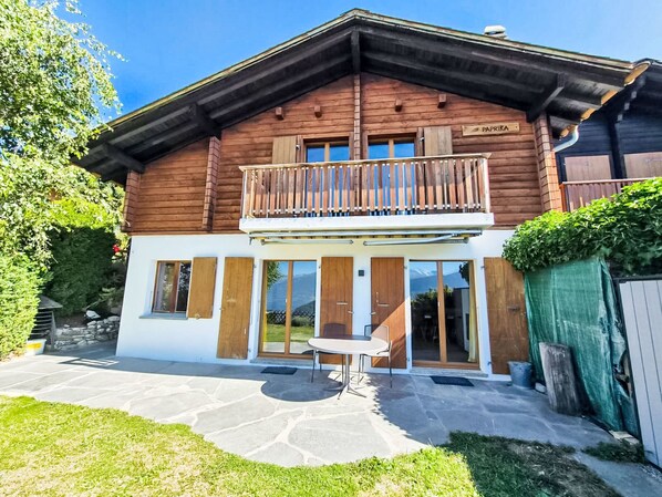 A wooden chalet with a balcony, a stone patio, and a view of the mountains. - Chalet Paprika by Interhome (Crans-Montana)