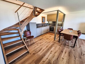 A modern kitchen with a wooden staircase, a dining area with chairs, and a kitchen island. - Chalet Paprika by Interhome (Crans-Montana)