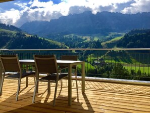 A wooden deck with a table and chairs overlooking a mountainous landscape.