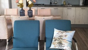 Una cucina moderna con mobili in legno chiaro, un fornello a gas e utensili pensili. In primo piano, due sedie blu con cuscino e un tavolo con un vaso di fiori.