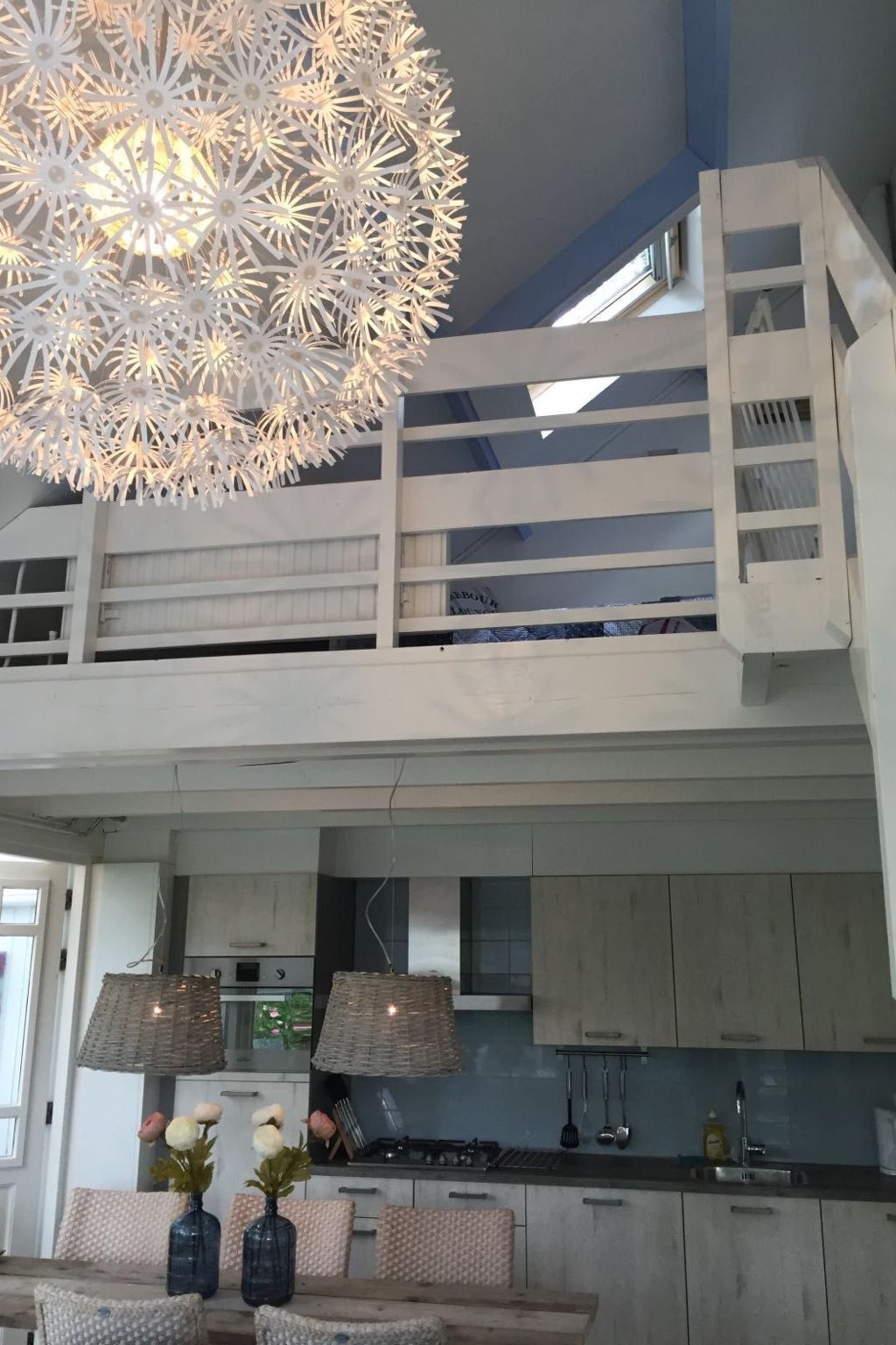 Een moderne keuken met een inbouwfornuis, een hanglamp en uitzicht op de verdieping erboven.