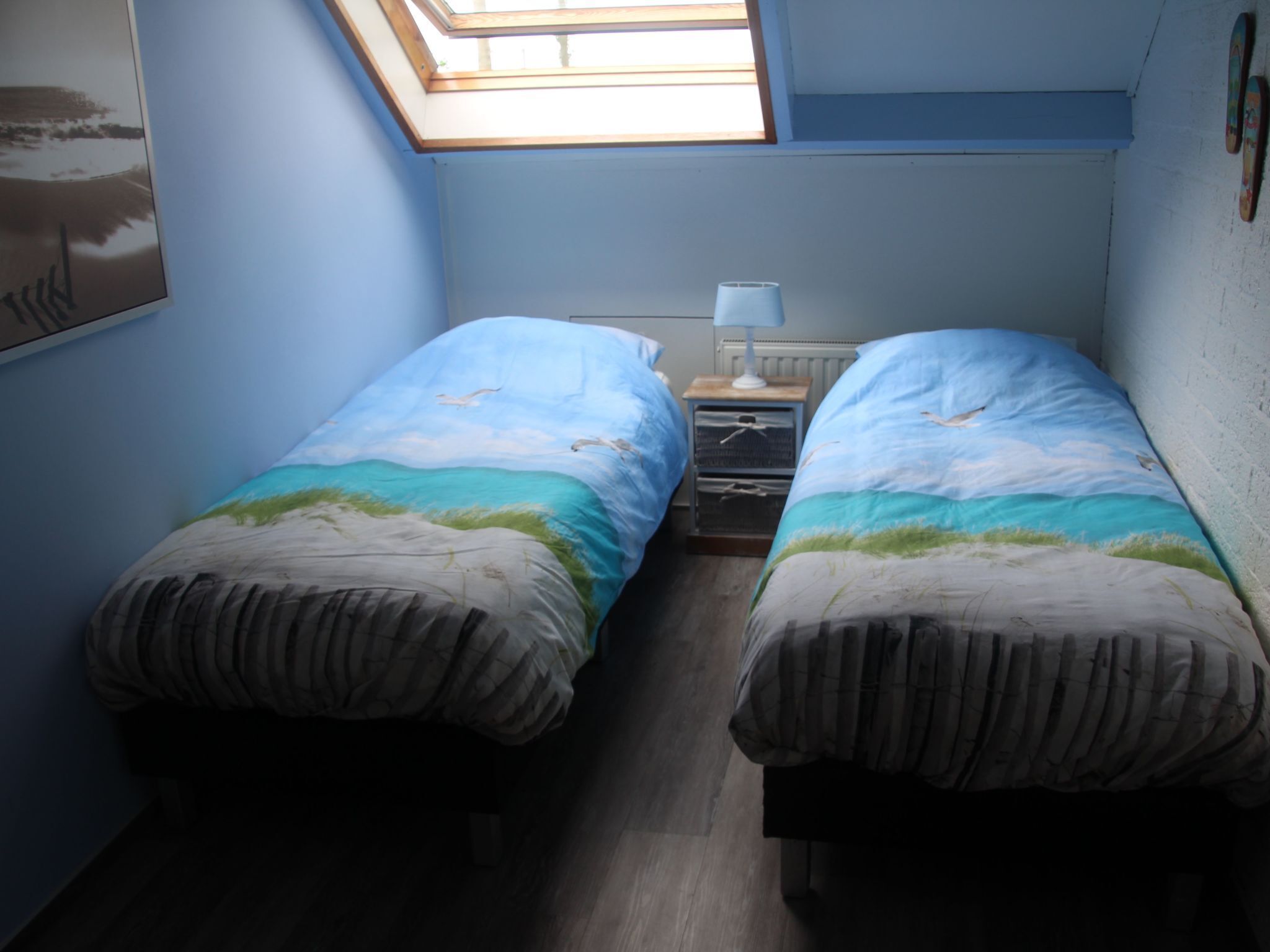 Una habitación pequeña con dos camas, un tragaluz, una mesita de noche y un radiador.