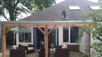 Een overdekt terras met tuinmeubilair en een glazen deur naar een woning.