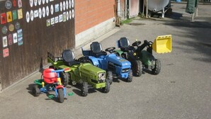 Une rangée de petits tracteurs est garée devant un bâtiment entouré d’une clôture en bois et orné de divers autocollants.