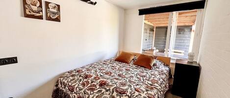 A bedroom with a bed, a window with blinds, and a wall-mounted shelf.