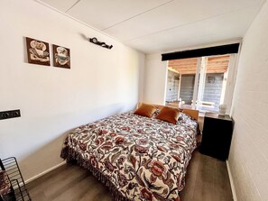 Une chambre avec un lit, une fenêtre avec des stores et une étagère fixée au mur.