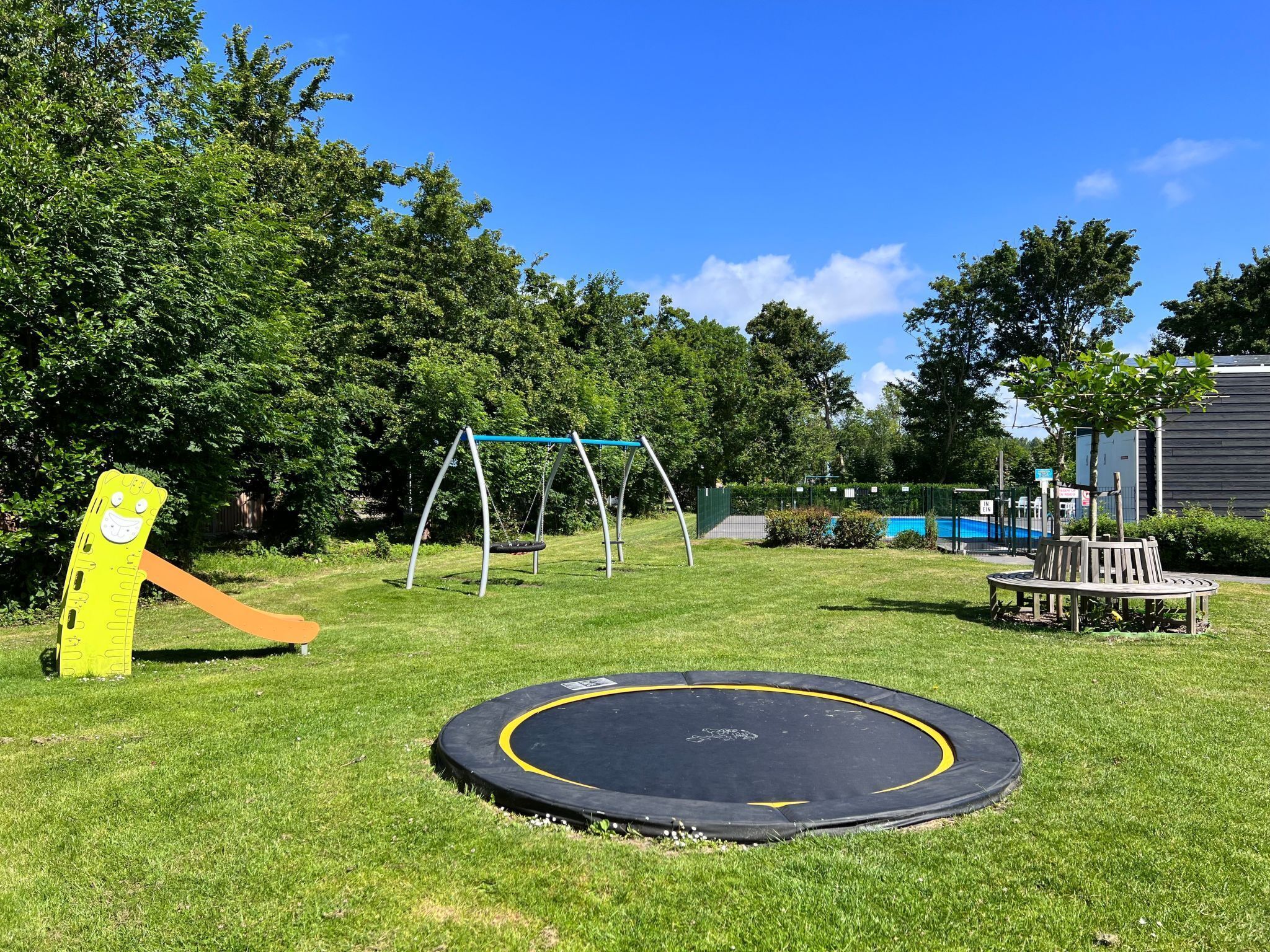 A playground with a swing set, a trampoline, and a slide.