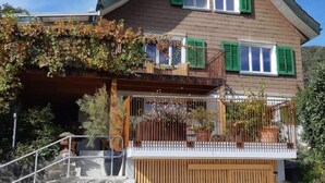 A two-story house with a wooden balcony, a stone wall in front, and a wooden garage door. - Seeblick by Interhome (Sarnen)