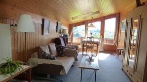 Interior acogedor de una cabaña con techo de madera, un sofá, una mesa de comedor y vistas al exterior.