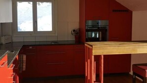 Moderni keittiö, jossa on punaiset kaapit, puinen keittiösaareke ja musta liesi.