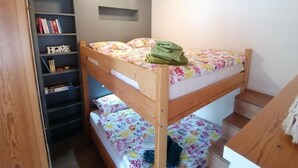 Habitación con literas, cabecera de madera, una estantería y un escritorio pequeño.