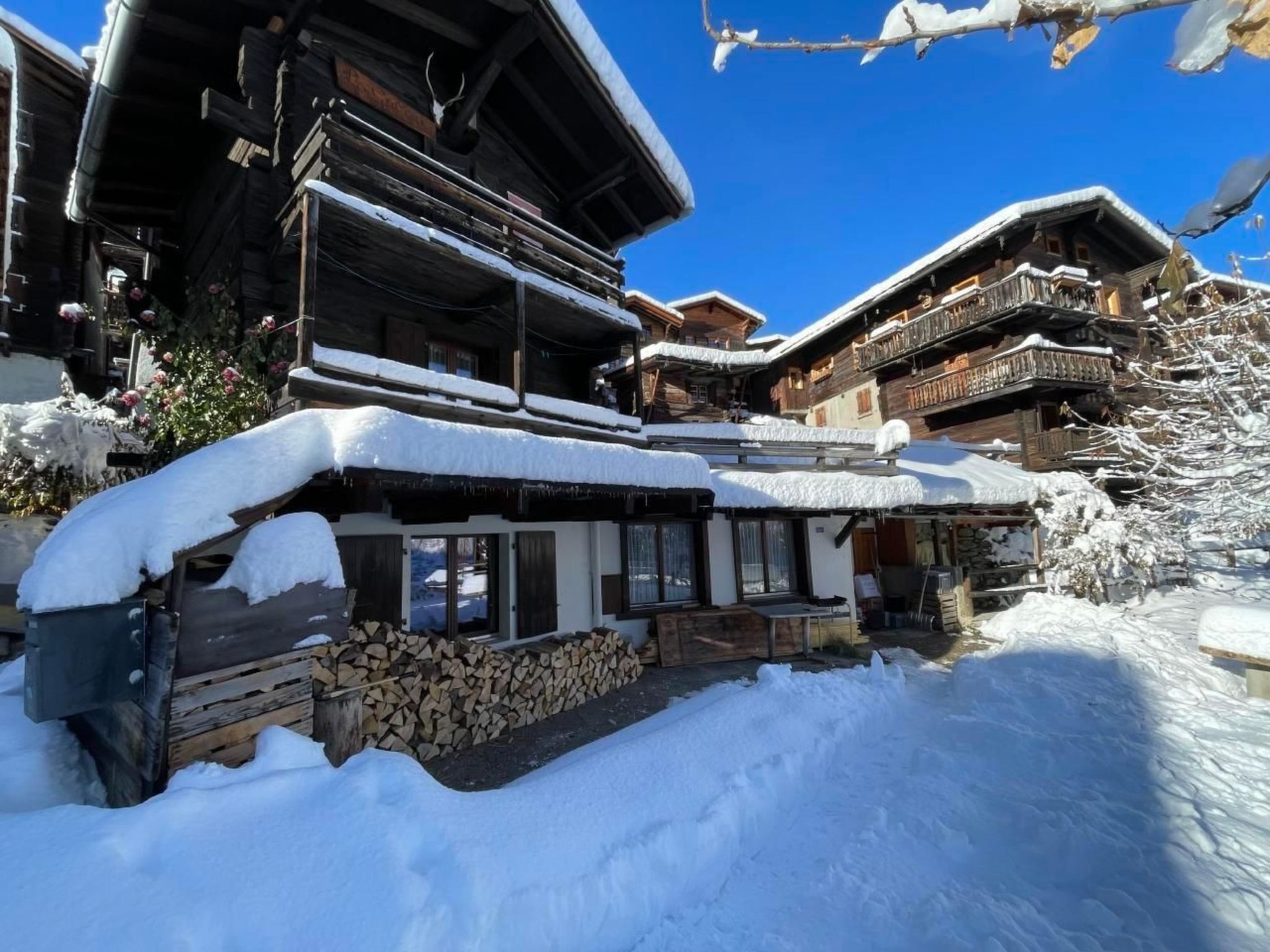Ein traditionelles Holzhäuschen mit schneebedecktem Dach, einer Holzdiele und einem Holzstoß davor.