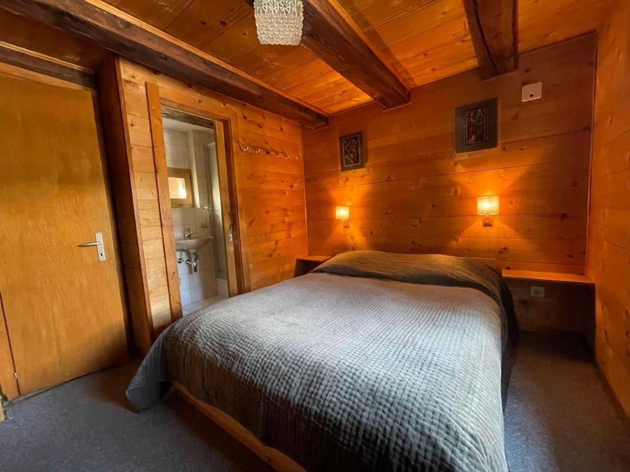 Ein Holzhütten-Zimmer mit einem Bett, einer Tür zu einem Badezimmer und zwei Wandleuchten.
