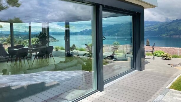 Una casa moderna con ampie vetrate che si affaccia su un lago e montagne.