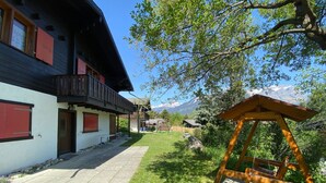 A two-story chalet with a balcony, a wooden swing set, and a mountain view. - Chalet Oase by Interhome (Leuk-Susten)
