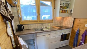A compact kitchen with wooden walls, a built-in oven, a sink, and a window with a view. - Chalet Oase by Interhome (Leuk-Susten)