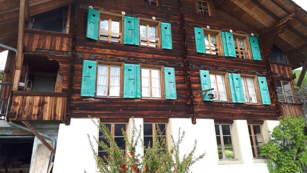 Een klassiek houten chalet met veel ramen en luiken, kenmerkend door een rustieke bouwstijl.