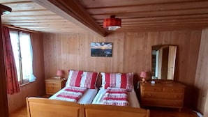 Een houten kamer met een tweepersoonsbed, twee nachtkastjes, een spiegel en een raam met gordijnen.