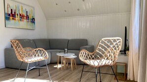 A modern living room with a grey sofa, two wicker chairs, a small white table, and a painting on the wall. - 162 Grachthaus by Interhome (Anjum)
