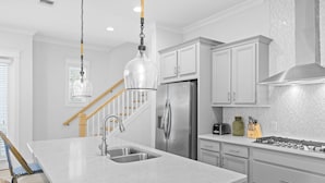 Une cuisine moderne dotée d’un îlot central, d’appareils électroménagers en acier inoxydable et d’un luminaire suspendu.