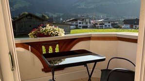 Een balkon met een tafel en stoelen, een bloemstuk en uitzicht op een vallei met huizen en bergen.