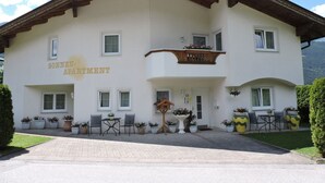 Een gebouw met twee verdiepingen, met het bord “SONNEN APARTMENT” dat aangeeft dat het een accommodatie is. Er zijn zitgedeeltes buiten met tafels en stoelen, en er staan bloempotten rond de ingang.