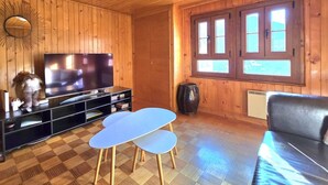 Una habitación con paneles de madera, un televisor, un sofá, una mesita y una ventana con persianas.