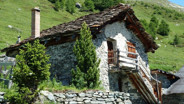 Una casa de piedra tradicional con un balcón de madera, con montañas al fondo.
