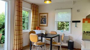 Ein Essbereich mit Tisch und vier Stühlen, einem Bild an der Wand und einem Fenster mit Vorhängen.