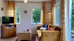 Ein gemütliches Wohnzimmer mit Fernseher, Holzschrank, Rattan-Couchtisch und einer Couch mit Kissen.